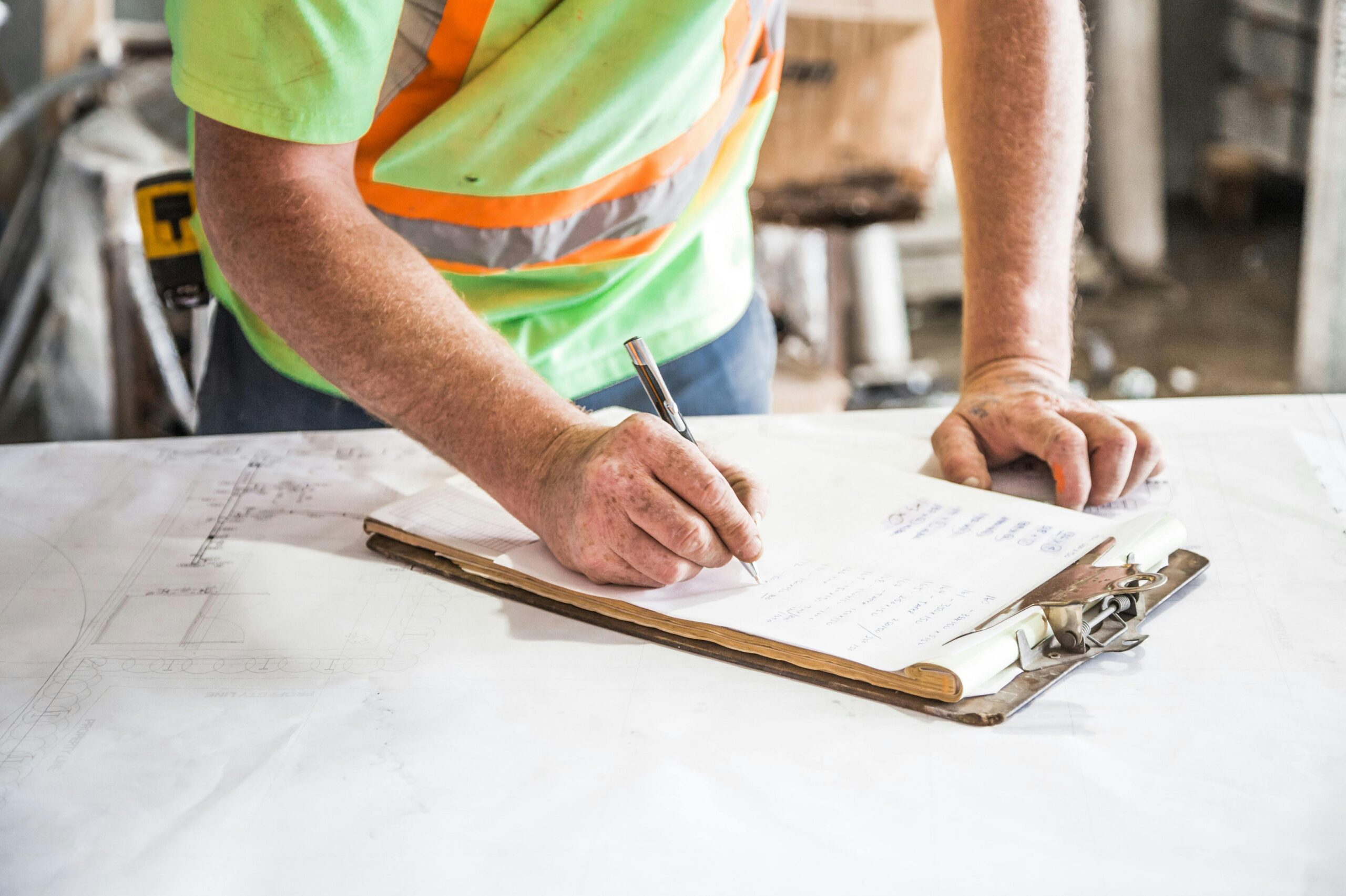This image depicts a builder reviewing a budget sheet on a clipboard. 