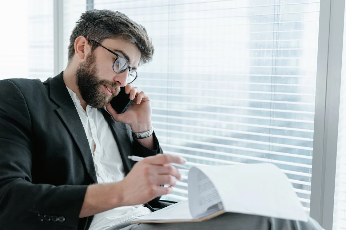 A banker is reviewing a loan application in an office while talking on the phone.