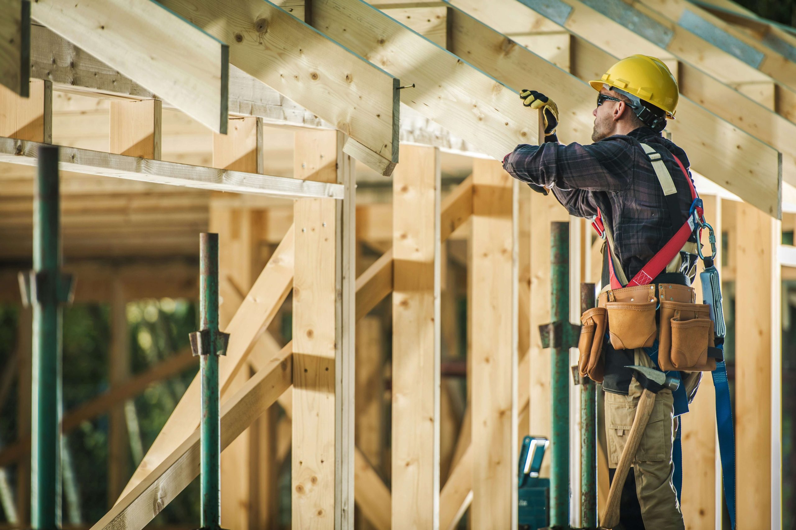 Construction worker in a yellow hard hat working on wood framing, illustrating the labor and materials that contribute to home building costs.